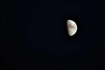 A waxing gibbous moon, with shadowed craters visible, contrasts against a black void.