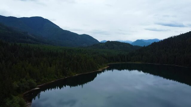 Fly over mirror-like lake on overcast day. Opening forest hills and mountains