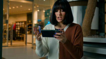 Funny 20s woman girl female gamer lady play with phone video game online playing lost championship failure feel anger annoyance with smartphone competitive cell gaming indoors emotional loose stress