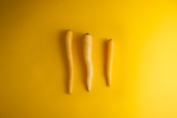 Yellow carrots arranged parallel to each other on a yellow background top view copy space
