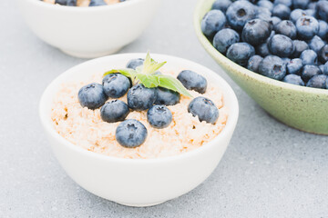 Oatmeal porridge garnished with blueberry and mint leaf in white bowl on the table. Morning superfood porridge recipe. Healthy breakfast ideas