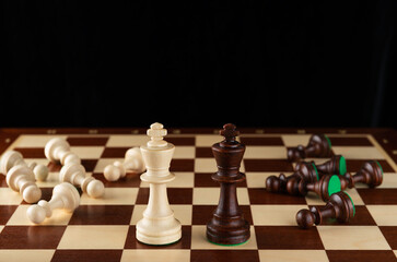 Wooden light and dark chess kings on a chessboard with lying pieces.