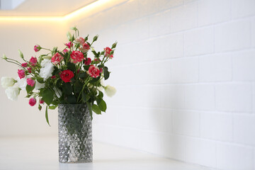 Vase with beautiful flowers on white countertop in kitchen, space for text