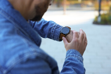 Man looking at watch outdoors, closeup. Being late concept