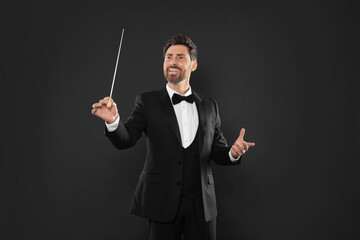 Happy professional conductor with baton on black background