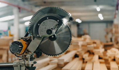 A angle saw in a factory house with a pile of wooden boards in the background