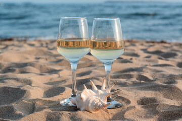 Glasses of tasty wine and seashell on sand near sea
