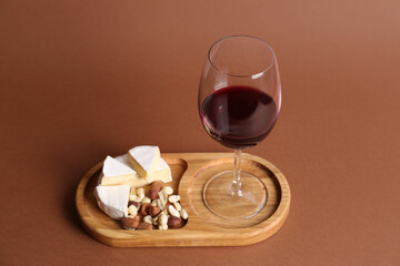 Glass of red wine, cheese and nuts on brown background