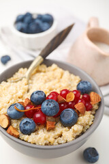 Bowl of delicious cooked quinoa with almonds, cranberries and blueberries on white table, closeup