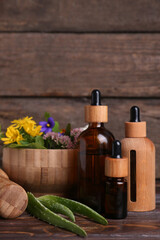 Glass bottles of aromatic essential oil and mortar with different herbs on wooden table