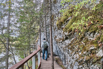 Senior male hiker walking on wooden hiking trail near cliff. Nature park Deer streams, Russia