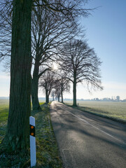 Landstra&szlig;e in der Wintersonne mit Dorf im Hintergrund