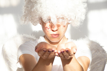 A young girl in an angel costume with wings and curly hair stretched out her hands forward on an...