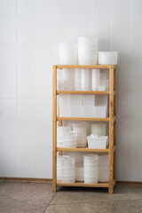Fototapeta na wymiar White plastic cheese forms, molding glasses on wooden shelves. Private small-scale cheese factory