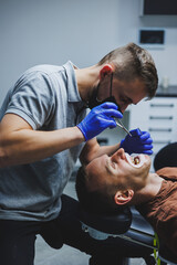 Orthodontic treatment of teeth. A young man at a dentist's appointment. The doctor installs metal...