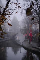 Utrecht, The Netherlands, November 29, 2022. Bridge over the Oudegracht canal in autumn fog. Red umbrellas.
