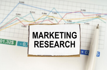 Against the background of business graphics and pens, a sign with the inscription - MARKETING RESEARCH