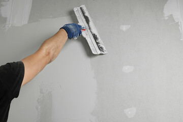 Professional worker plastering wall with putty knife, closeup