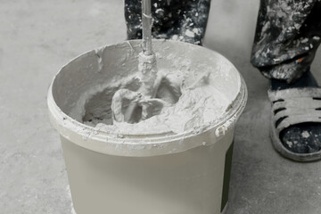 Professional worker mixing plaster in bucket indoors, closeup