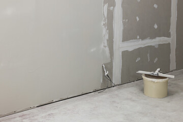 Bucket with putty knife near plastered wall indoors