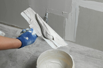 Professional worker holding putty knife with plaster indoors, closeup