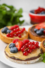 Fresh rice cake and rusks with different toppings served on white plate, closeup