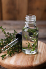 Bottle of thyme essential oil and fresh plant on wooden board, closeup