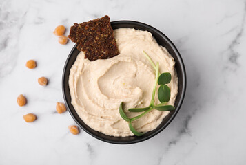 Bowl of delicious hummus with crispbread on white marble table, flat lay