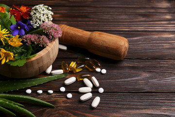 Mortar with fresh herbs, flowers and pills on wooden table, space for text