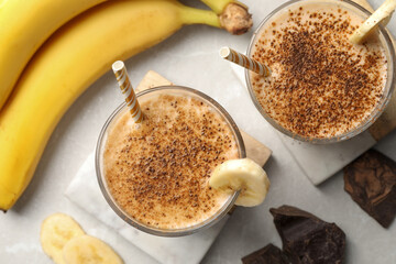Tasty banana smoothie, fresh fruits and chocolate on white marble table, flat lay