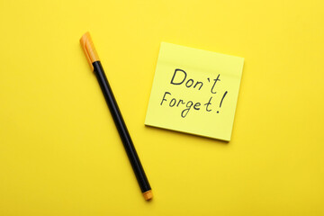 Paper note with phrase Don' t Forget and pen on yellow background, flat lay