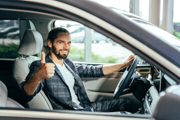 Happy caucasian man sitting in car gesturing thumbs up. Handsome man sitting inside modern car and...