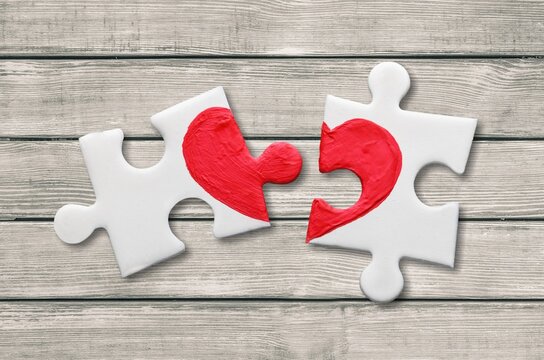 closeup of two pieces of a puzzle forming a heart on a wooden surface,