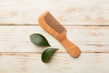 Hair comb with green leaves wooden on background. Top view