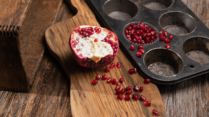 Pomegranate fruit arias on a wooden cutting board on a table.