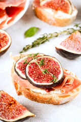 Toast with fig, cream cheese, prosciutto, walnuts and honey on white concrete table. Healthy quick breakfast recipe. Vertical image. Selective focus