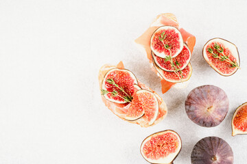 Healthy quick breakfast - toasts with fresh ripe fig, cheese, prosciutto and herbs over white concrete table background with copy space. Top view, selective focus