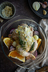 Raw coquelet jaune (yellow spring chicken) with oranges, onions and herb butter in glass baking dish.