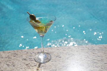 COLD MARTINI GLASS WITH OLIVES ON THE SHORES OF A POOL ON A SUNNY DAY