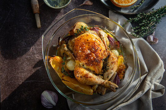 Oven roasted coquelet jaune (yellow spring chicken) with oranges, onions and herb butter in glass baking dish.