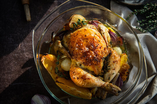 Oven roasted coquelet jaune (yellow spring chicken) with oranges, onions and herb butter in glass baking dish.