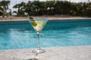COLD MARTINI GLASS WITH OLIVES ON THE SHORES OF A POOL ON A SUNNY DAY
