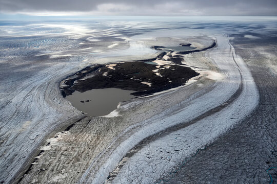 A giant glacier flows down from off the ice cap towards the coast exposing a circular area of rock.; Greenland.