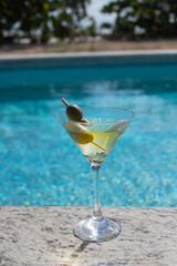 COLD MARTINI GLASS WITH OLIVES ON THE SHORES OF A POOL ON A SUNNY DAY