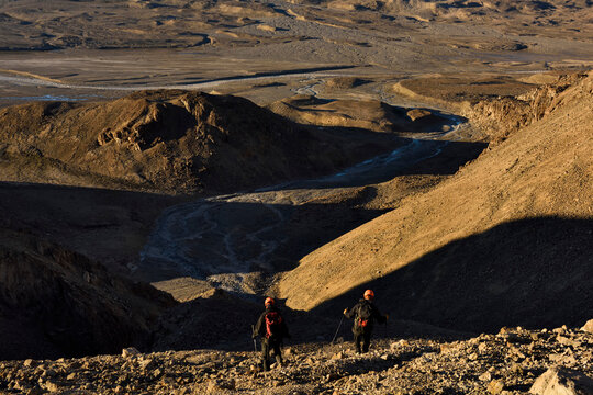 Expedition team members skip down one of the scree slopes of rocks towards the bottom of the valley of the caves and then onto camp to put a pan of water on the stove for tea.