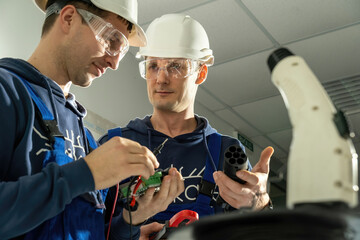 Workers work with cables for EV charging plug and discuss ways for soldering wires. Electricians...