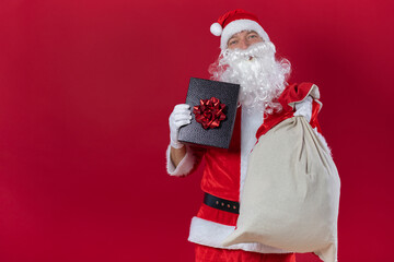 Portrait von einem verkleideten Weihnachtsmann mit Geschenk, isoliert auf roten Hintergrund im...