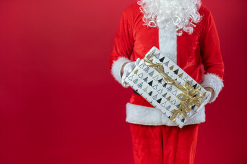 Nahaufnahme von der Hand von einem Weihnachtsmann, der ein Geschenk, vor roten Hintergrund, hält....