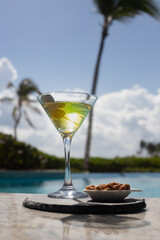COLD MARTINI GLASS WITH OLIVES AND PEANUTS ON THE SHORES OF A POOL ON A SUNNY DAY