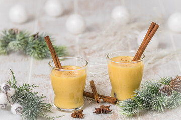 Obraz na płótnie Canvas Two glasses of eggnogg with cinnamon sticks on white wooden background, christmas. Auld Man's milk, Coquito or Creme de Vie or Eierlikör.